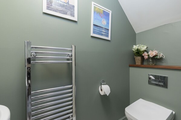 A bathroom with a chrome towel rack, a toilet, a framed picture on the wall, and a small shelf with flowers.