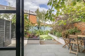 A patio area with a table and chairs, a small lawn, and a brick wall.
