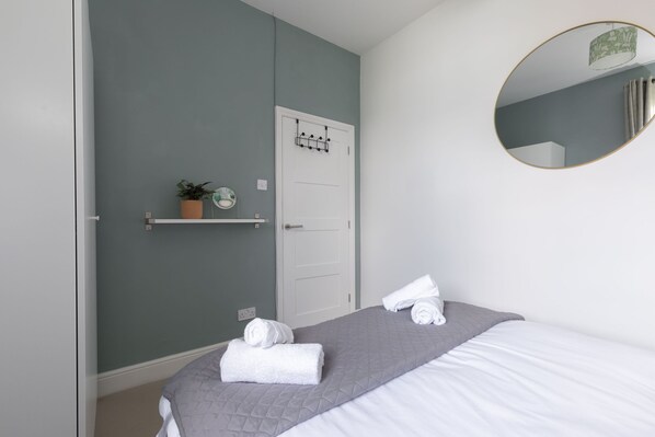 A bedroom with a bed, a mirror, a door, and a shelf with a plant.