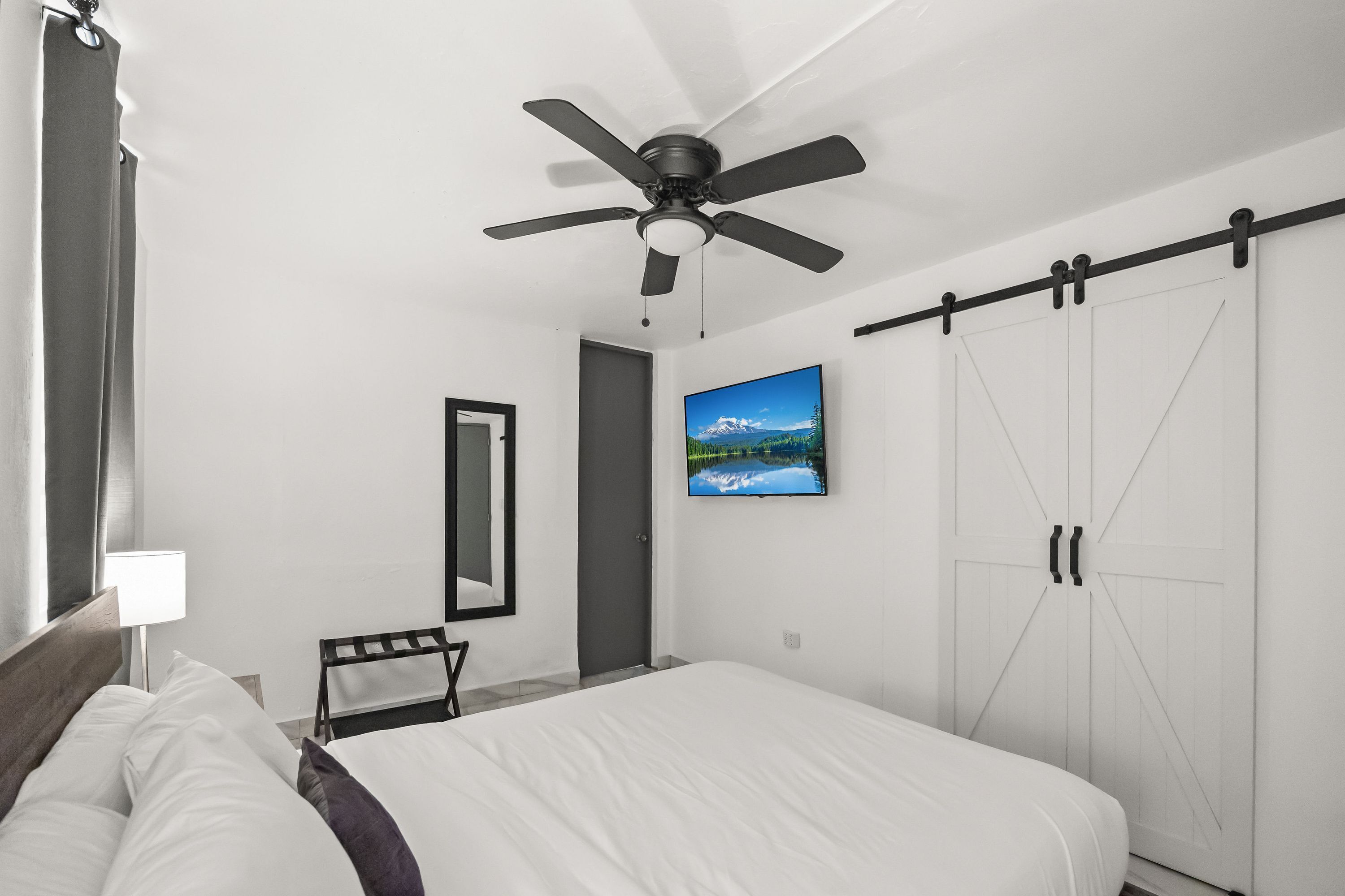 A bedroom with a bed, a ceiling fan, a mounted TV, a wardrobe, and a door.