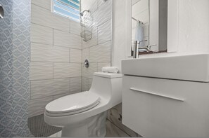 A modern bathroom with a white toilet, a shower with a glass door, and a sink with a mirror above it.