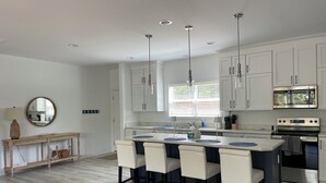 A modern kitchen with white cabinets, a central island with bar stools, stainless steel appliances, and pendant lighting. - Lake Norman Family Friendly Home with Dock in Denver NC (Denver)