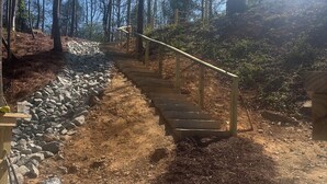 A wooden staircase leading up a hill, surrounded by trees and a stone wall. - Lake Norman Family Friendly Home with Dock in Denver NC (Denver)
