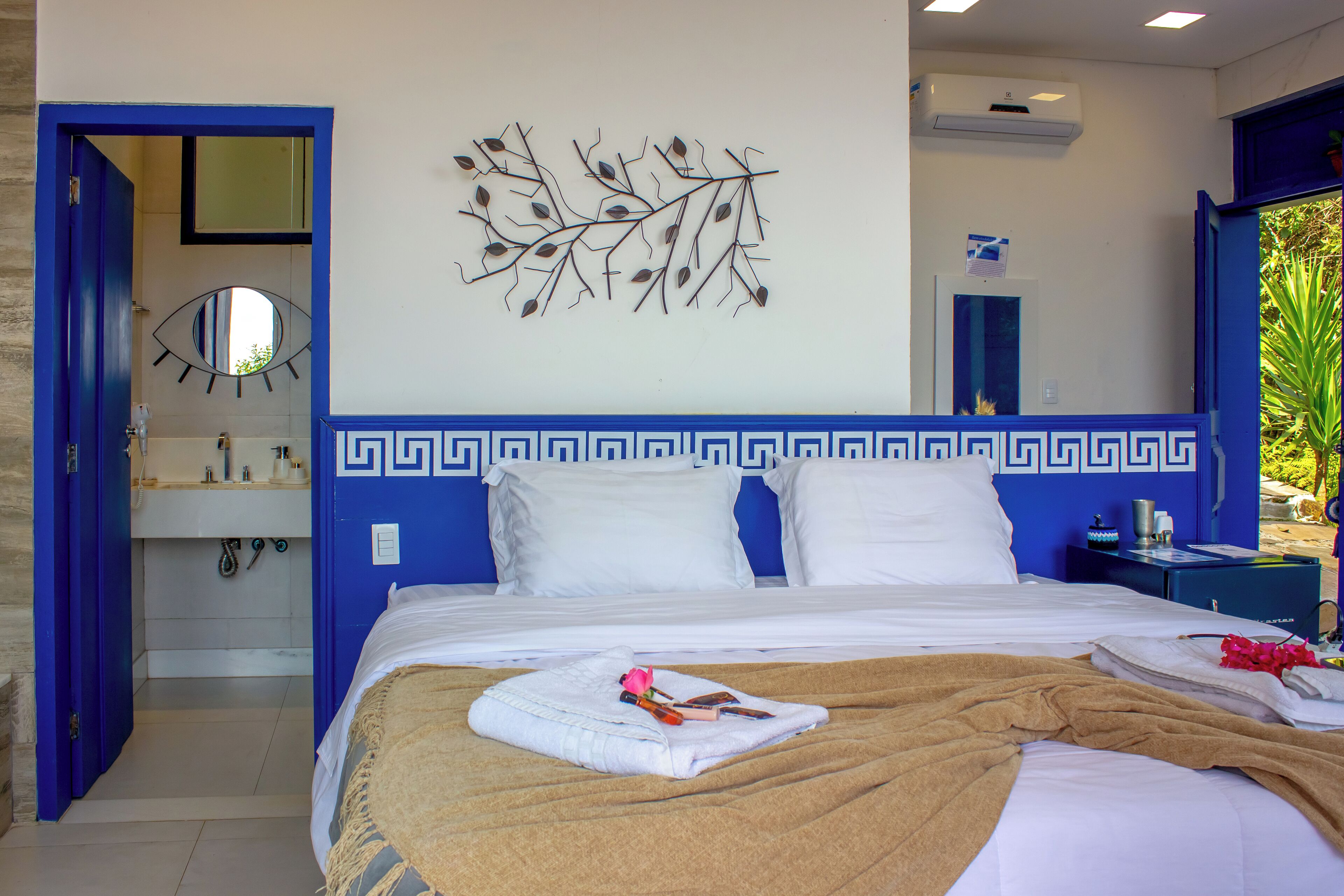 A hotel room with a bed, a bathroom with a mirror, and a wall decoration.
