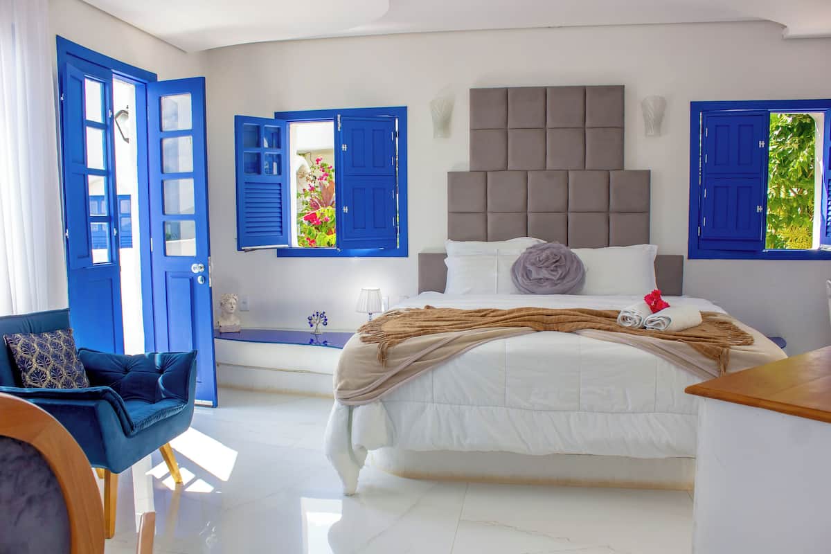 Ein Schlafzimmer mit einem Bett, einem Sessel und zwei Fenstern mit blauen Fensterläden.