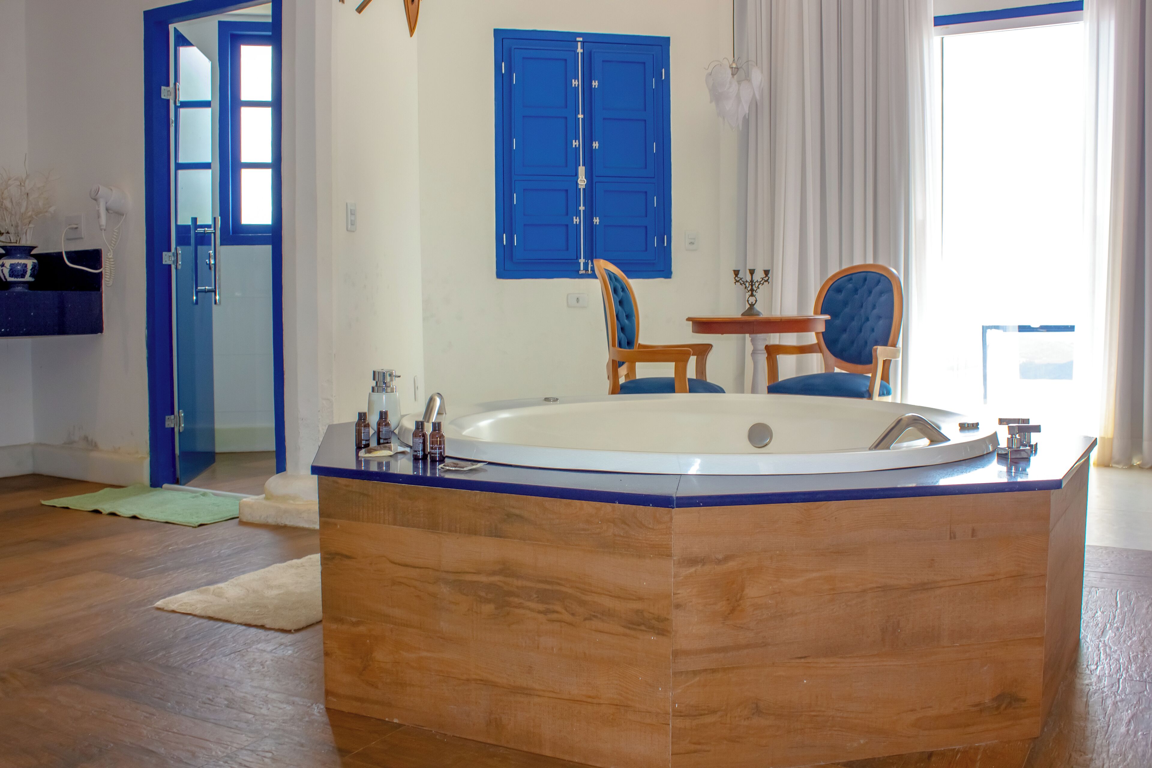 A modern bathroom with a freestanding bathtub, wooden floor, and a blue door.
