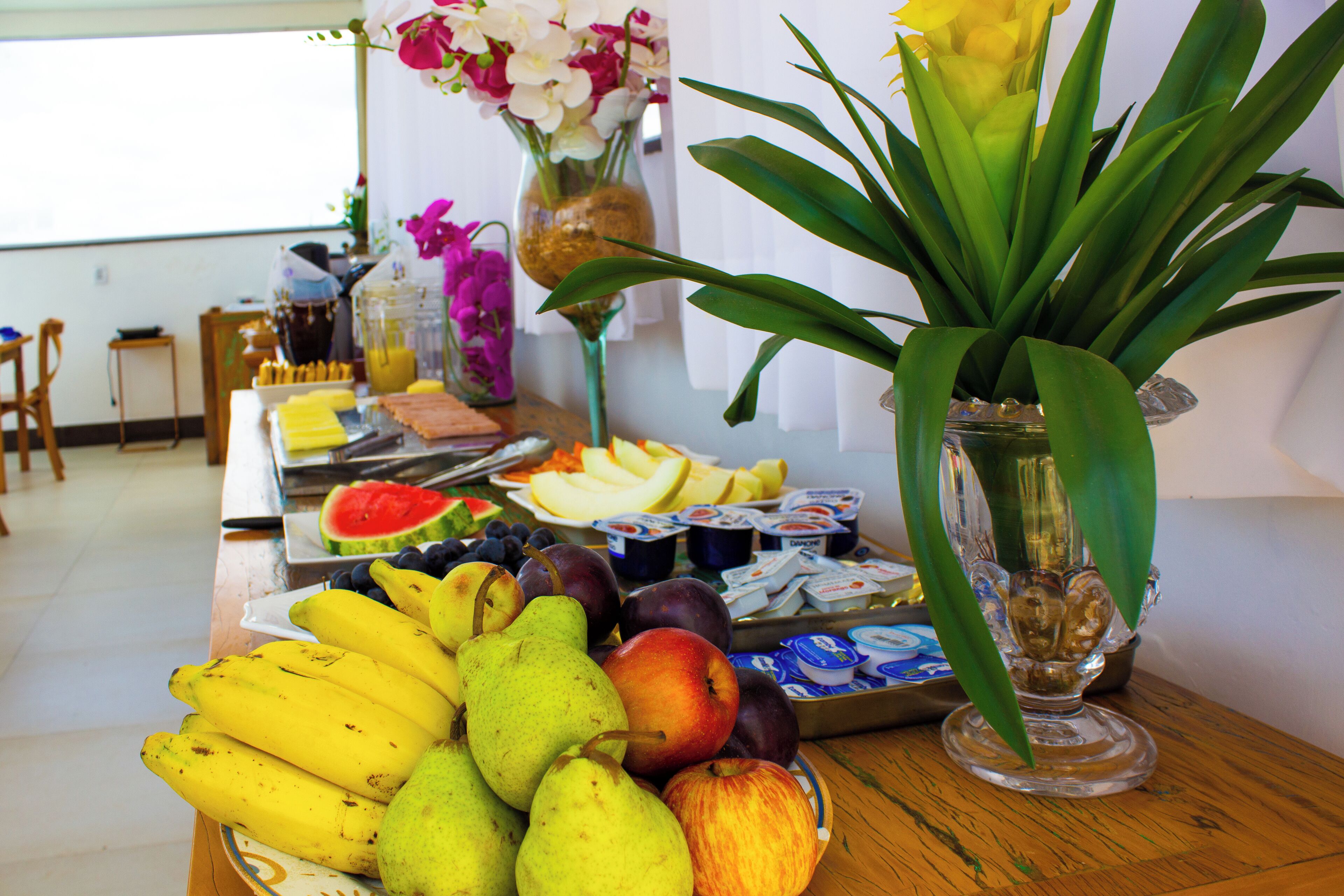 A table with fruits, yogurt, and a vase with flowers.
