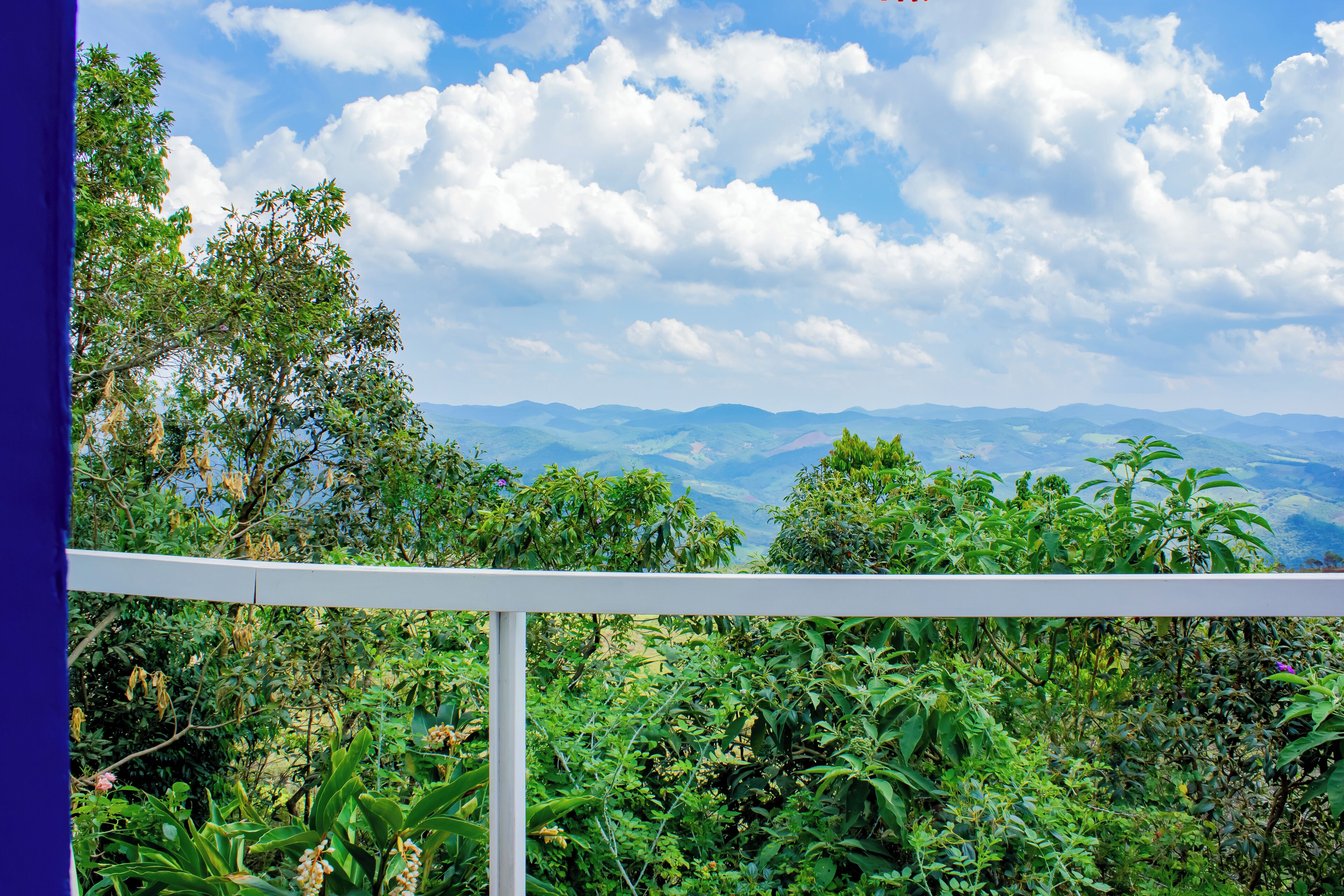 A balcony with a view of lush greenery and distant mountains under a partly cloudy sky.