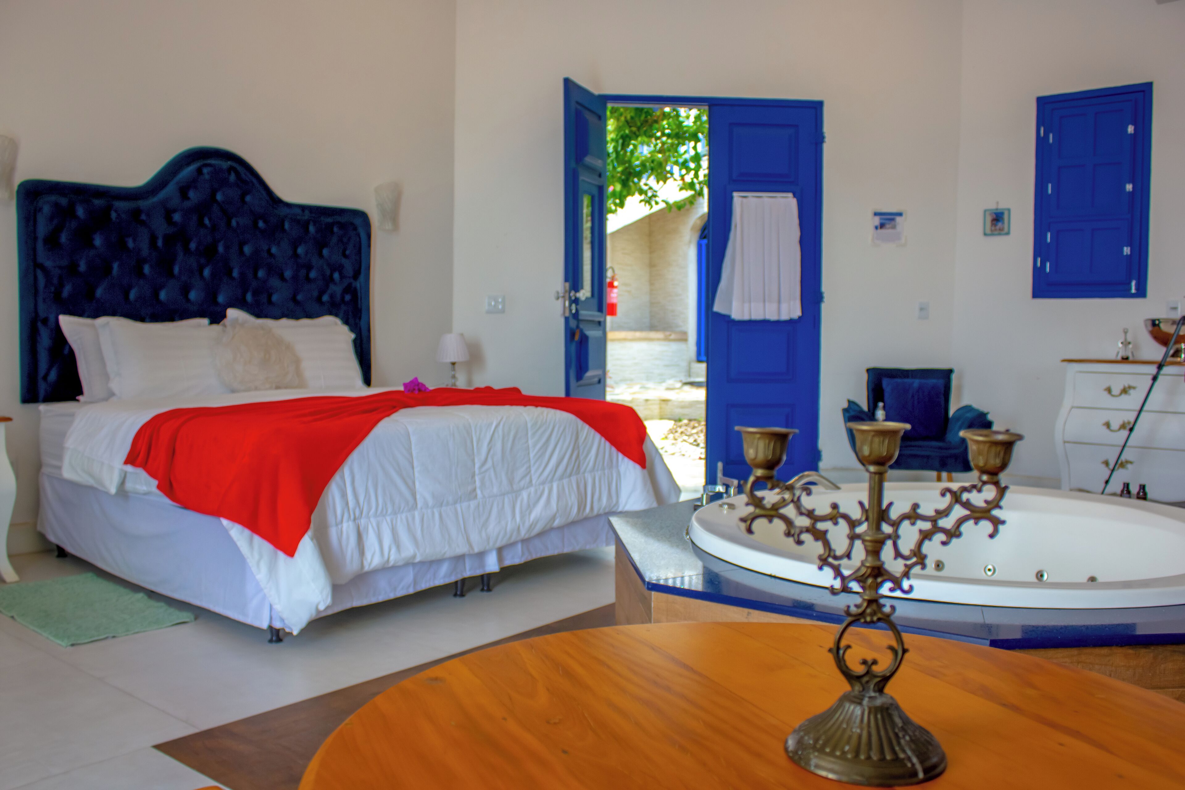 Quarto com cama, mesa de madeira redonda, banheira e portas azuis.