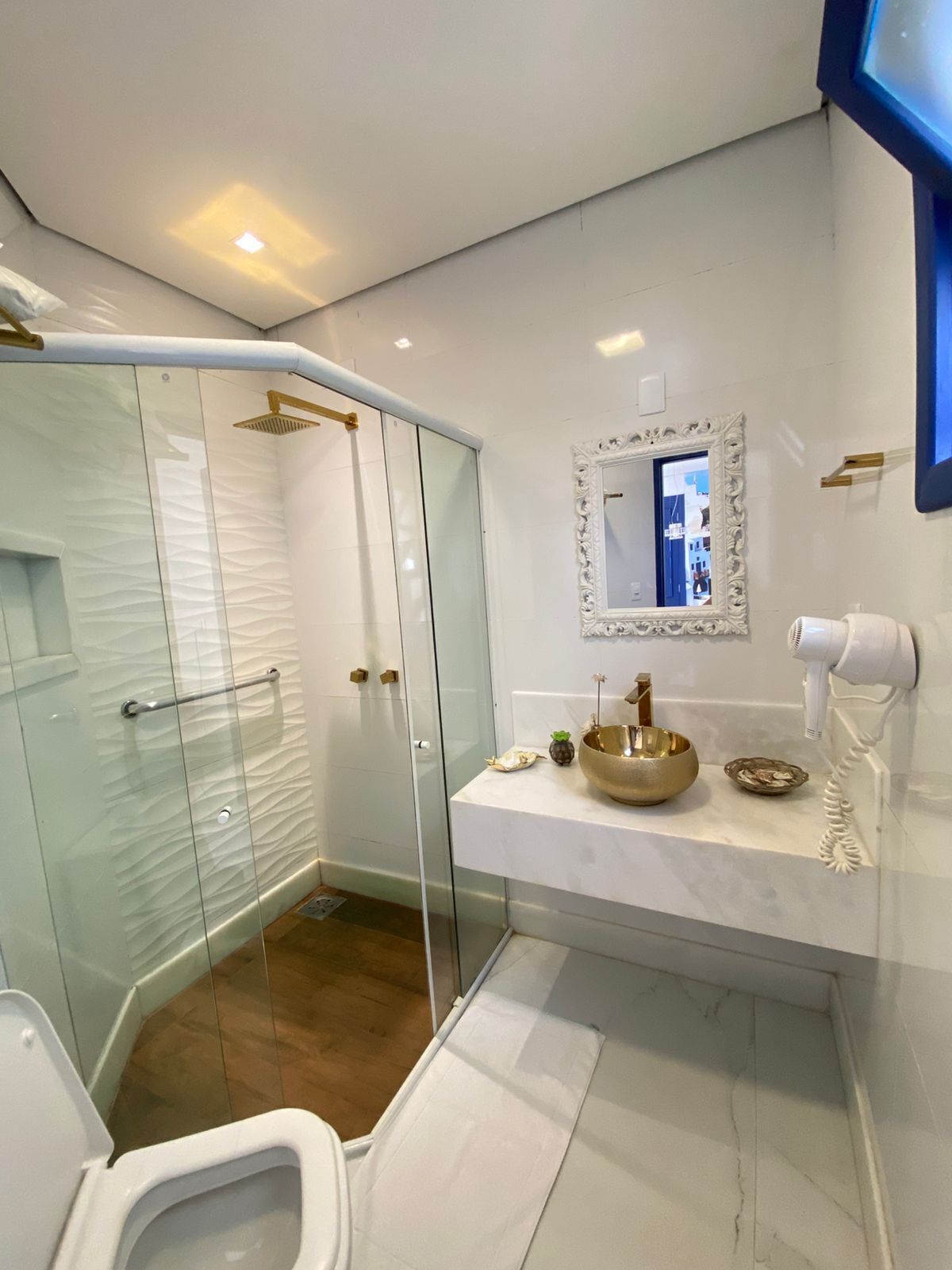 A modern bathroom with a glass shower enclosure, a white toilet, a vanity with a gold bowl, and a mirror with an ornate frame.