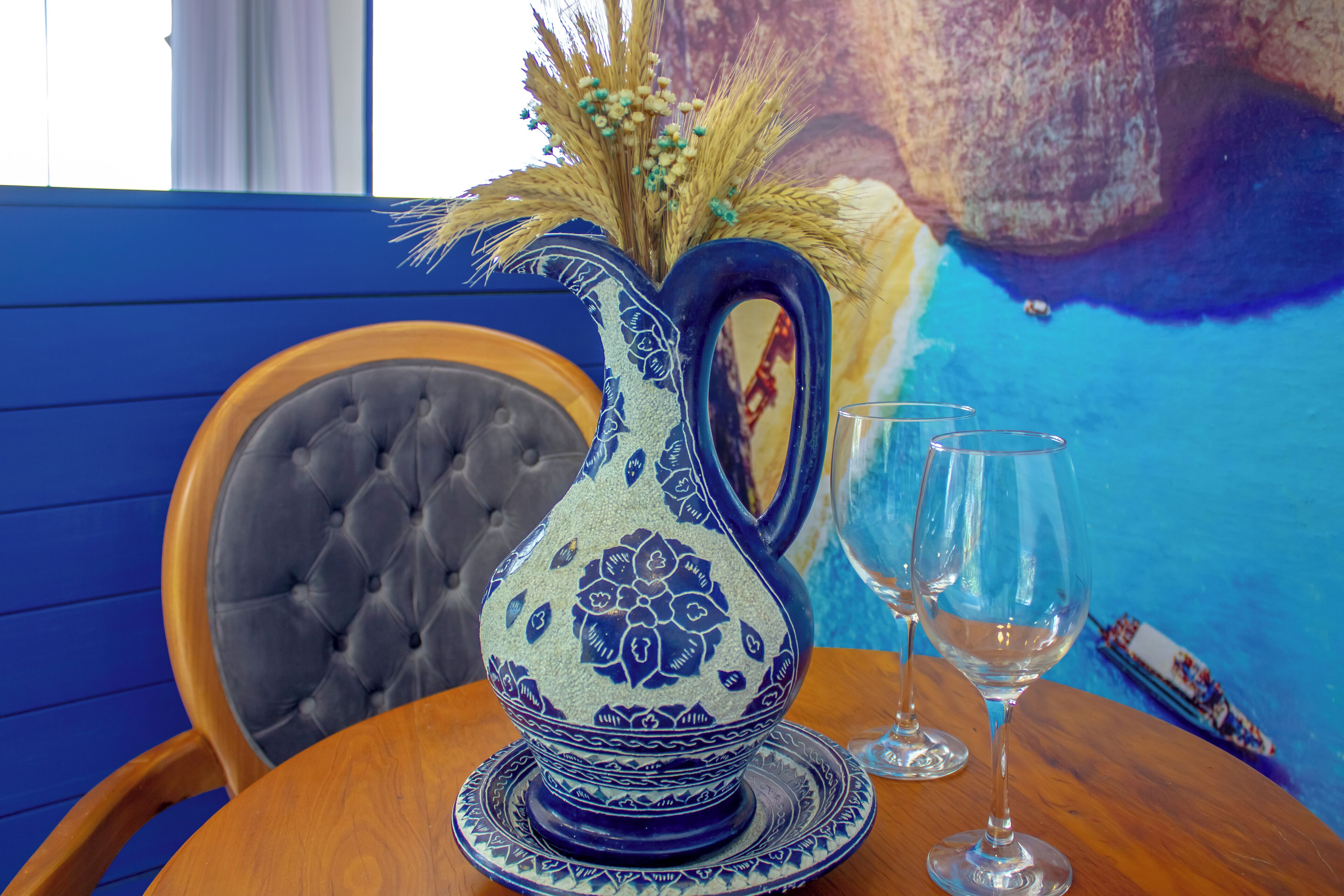 A table with a decorative pitcher, two wine glasses, and a blue and white patterned plate.