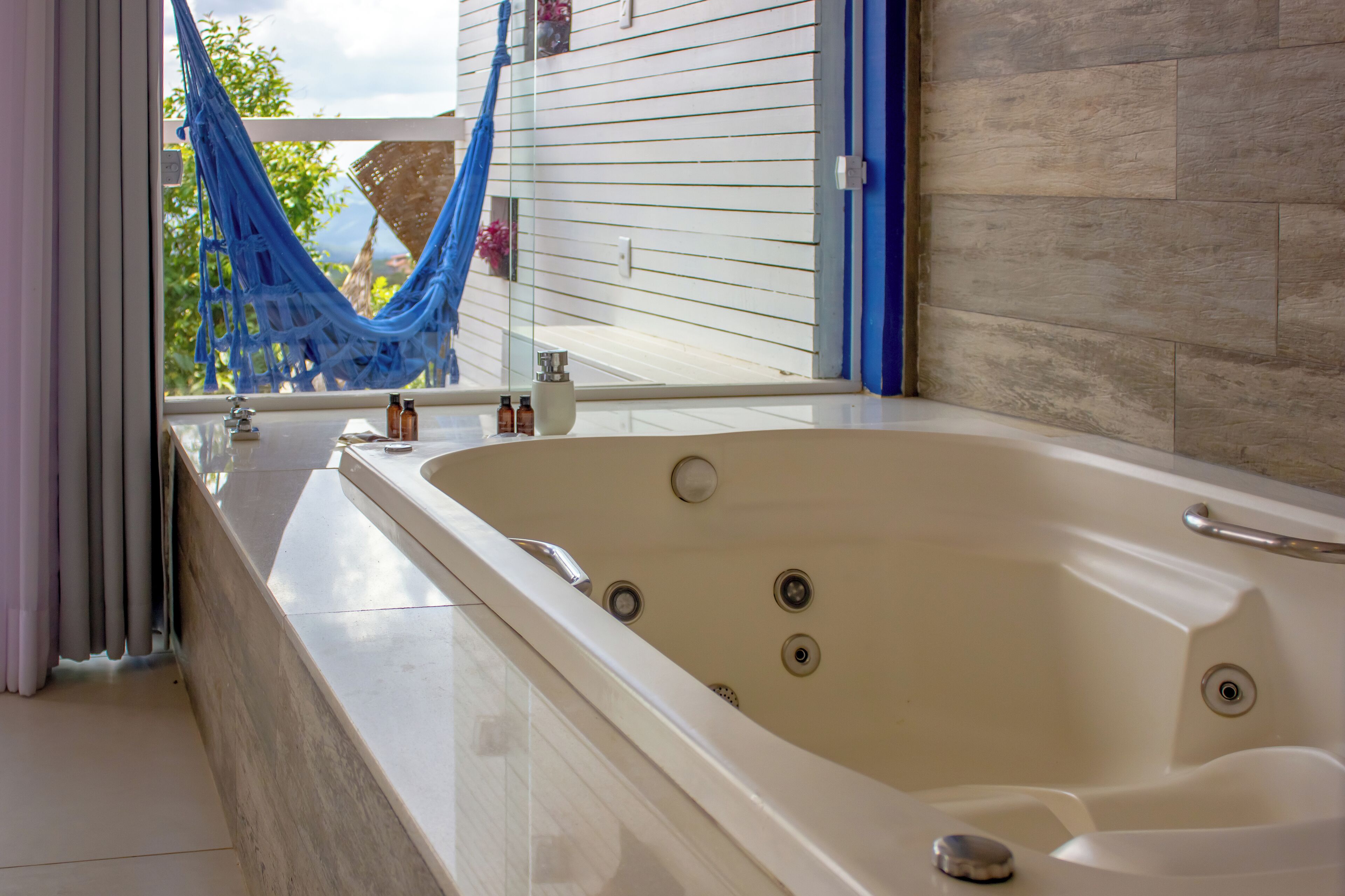 Une grande baignoire dotée d’une porte en verre, une fenêtre donnant sur les arbres et une serviette bleue accrochée à la porte.