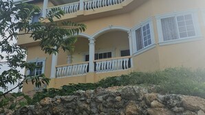 A multi-story building with balconies, a stone wall in the foreground, and a clear sky.