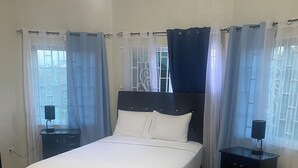 A bedroom with a bed, two nightstands, a black furry rug, and a window with curtains.
