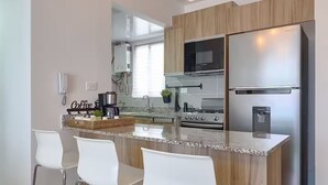 Une cuisine moderne dotée d’un îlot central, d’appareils électroménagers en acier inoxydable et de luminaires suspendus.