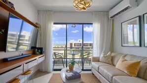 Un salon moderne comprenant un canapé, une table basse, un téléviseur et un balcon offrant une vue sur les immeubles.