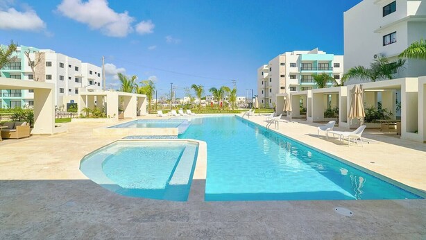 Un espace piscine comprenant plusieurs bassins, des chaises longues et un bâtiment moderne doté de balcons.