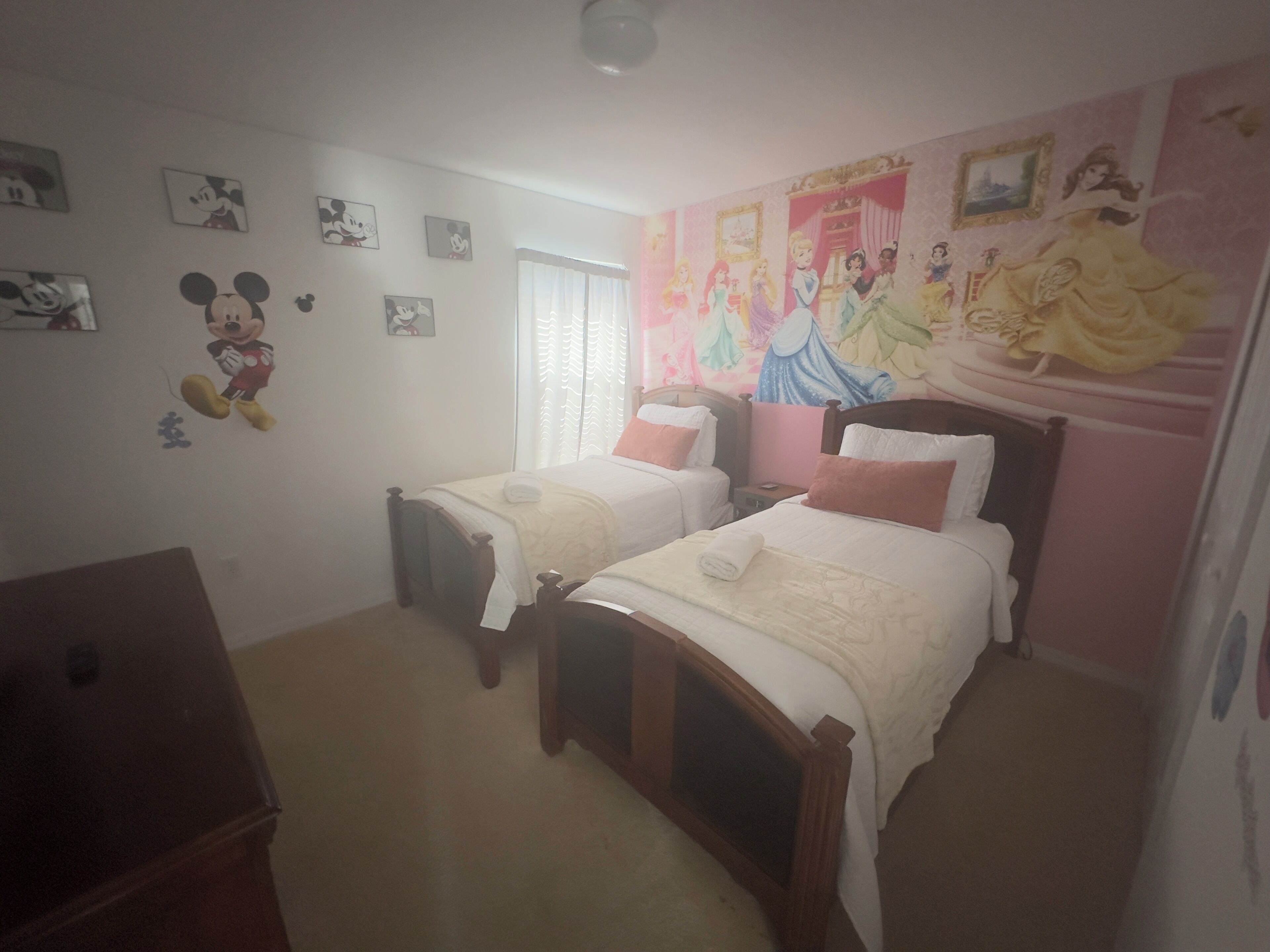 Une chambre avec deux lits, une commode et des décorations murales, notamment des motifs de Mickey Mouse et des princesses Disney.
