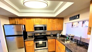 A modern kitchen with wooden cabinets, stainless steel appliances, and a granite countertop. - Direct Oceanfront 3-bedroom Condo in Cocoa Beach (Cocoa Beach)