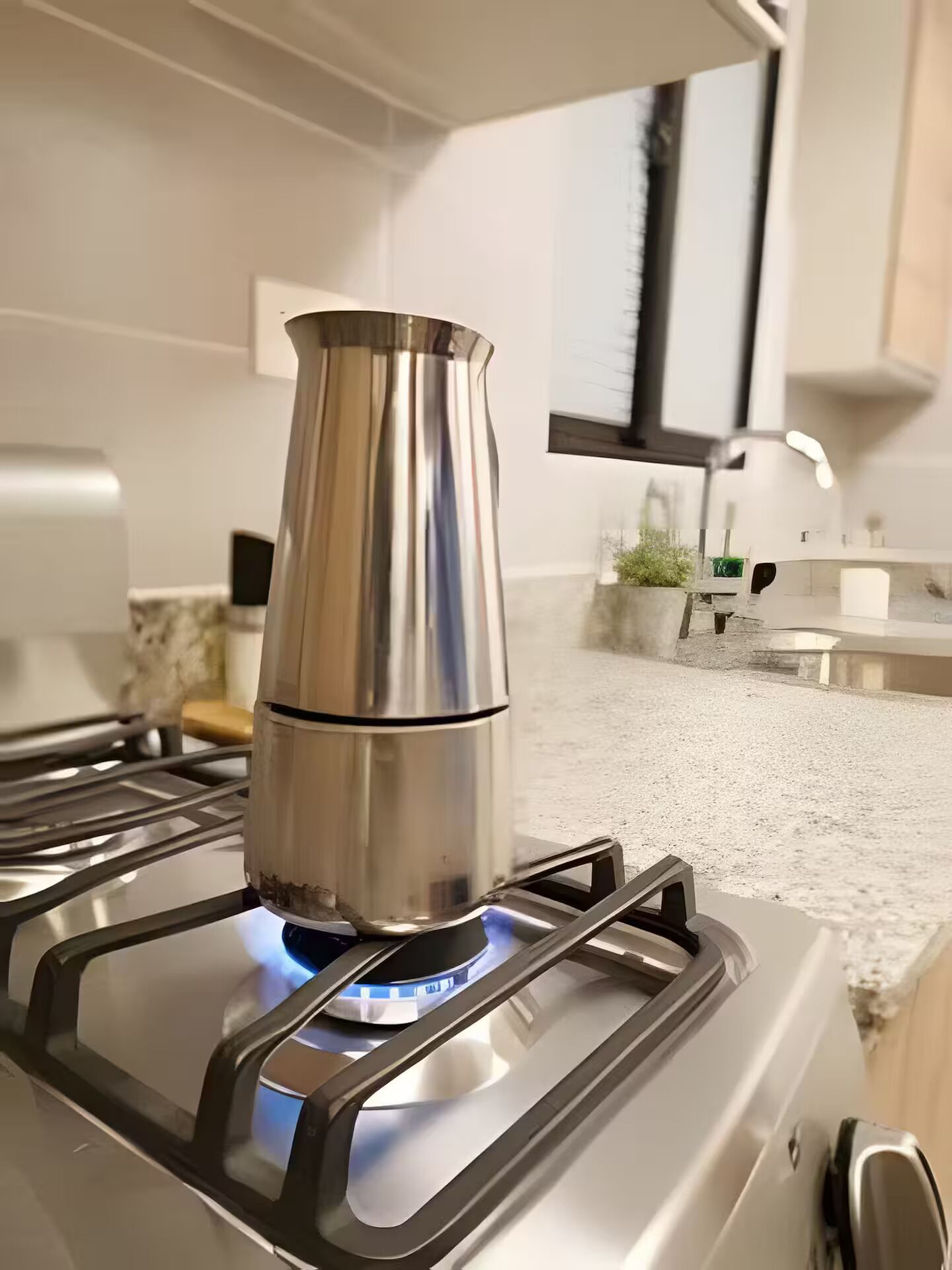 A stainless steel kettle on a modern stove with a blue flame.