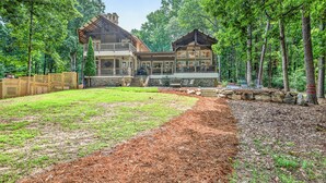 Un grand chalet à deux étages, doté de fondations en pierre et d’étages supérieurs en bois, entouré d’une forêt dense.