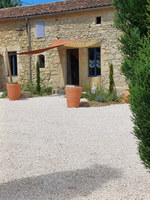 A stone building with a gravel driveway, two large terracotta planters, and a wooden pergola.