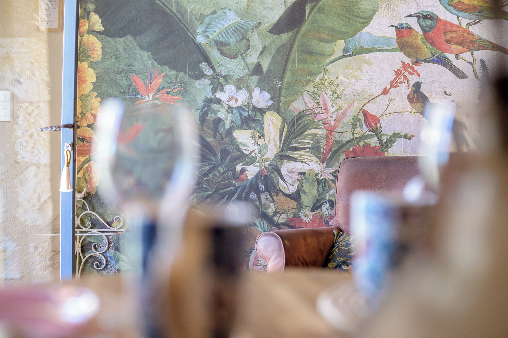 Quarto com um mural de pássaros e flores na parede, um portão de metal e uma poltrona de couro marrom.