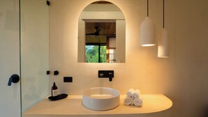 Ein modernes Badezimmer mit einem runden Waschbecken, einem Spiegel und einem Deckenventilator.