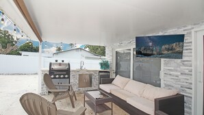 En udendørs terrasse med sofa, stole, bord og grill.
