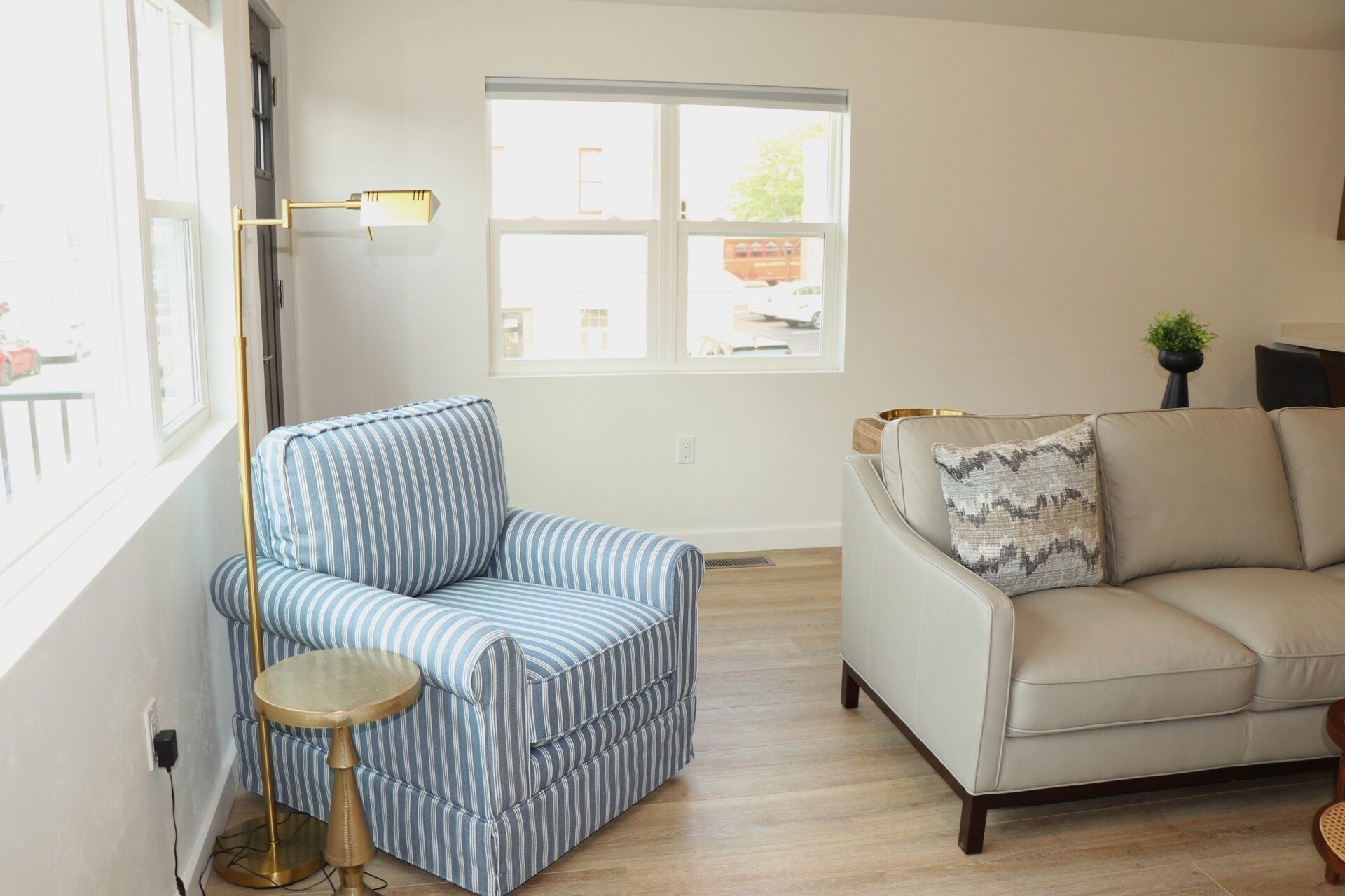 Una sala de estar con un sillón a rayas, un sofá color beige, una mesita redonda y una lámpara de pie.