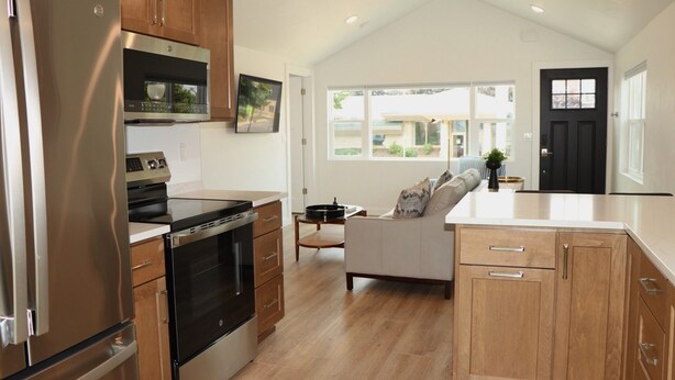 A modern kitchen with wooden cabinets, a stainless steel refrigerator, a built-in oven, and a large window offering a view of the outside.