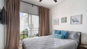 Une chambre avec un grand lit, un balcon agrémenté de rideaux et trois œuvres d’art encadrées accrochées au mur.