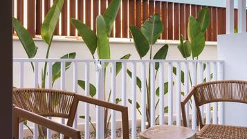 Een balkon met rieten stoelen, een ronde tafel, een witte balustrade en grote groene planten.