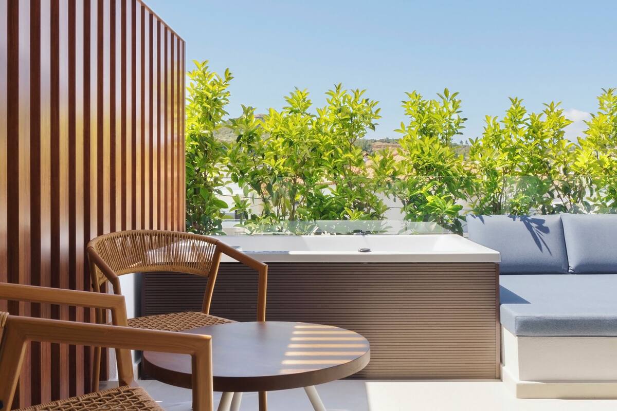 Un patio moderno al aire libre con una pérgola de madera, una mesa redonda, dos sillas de mimbre, un sofá y vistas a zonas verdes.