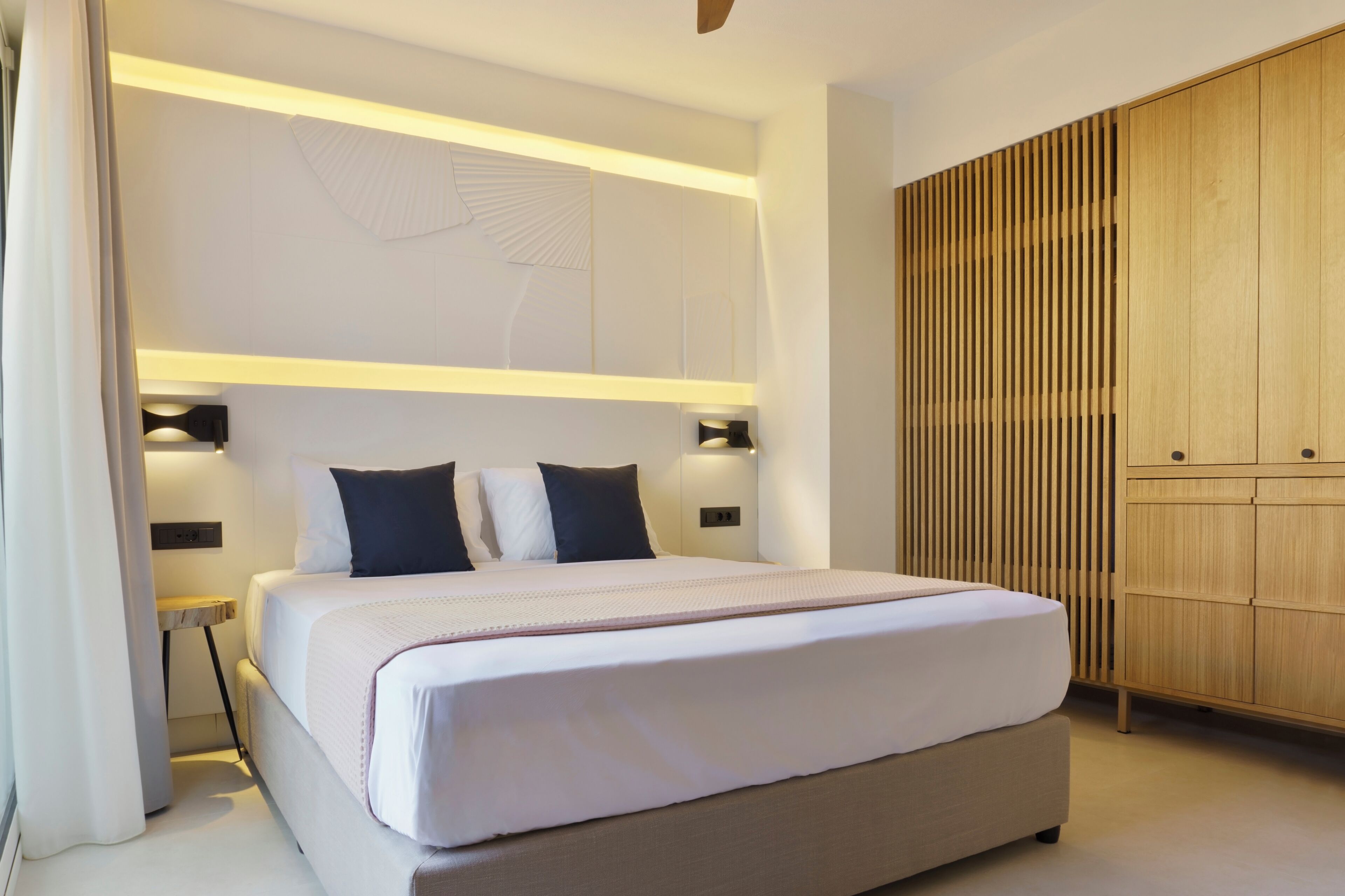 A modern hotel room with a large bed, bedside tables, a wardrobe, and a decorative wall panel.