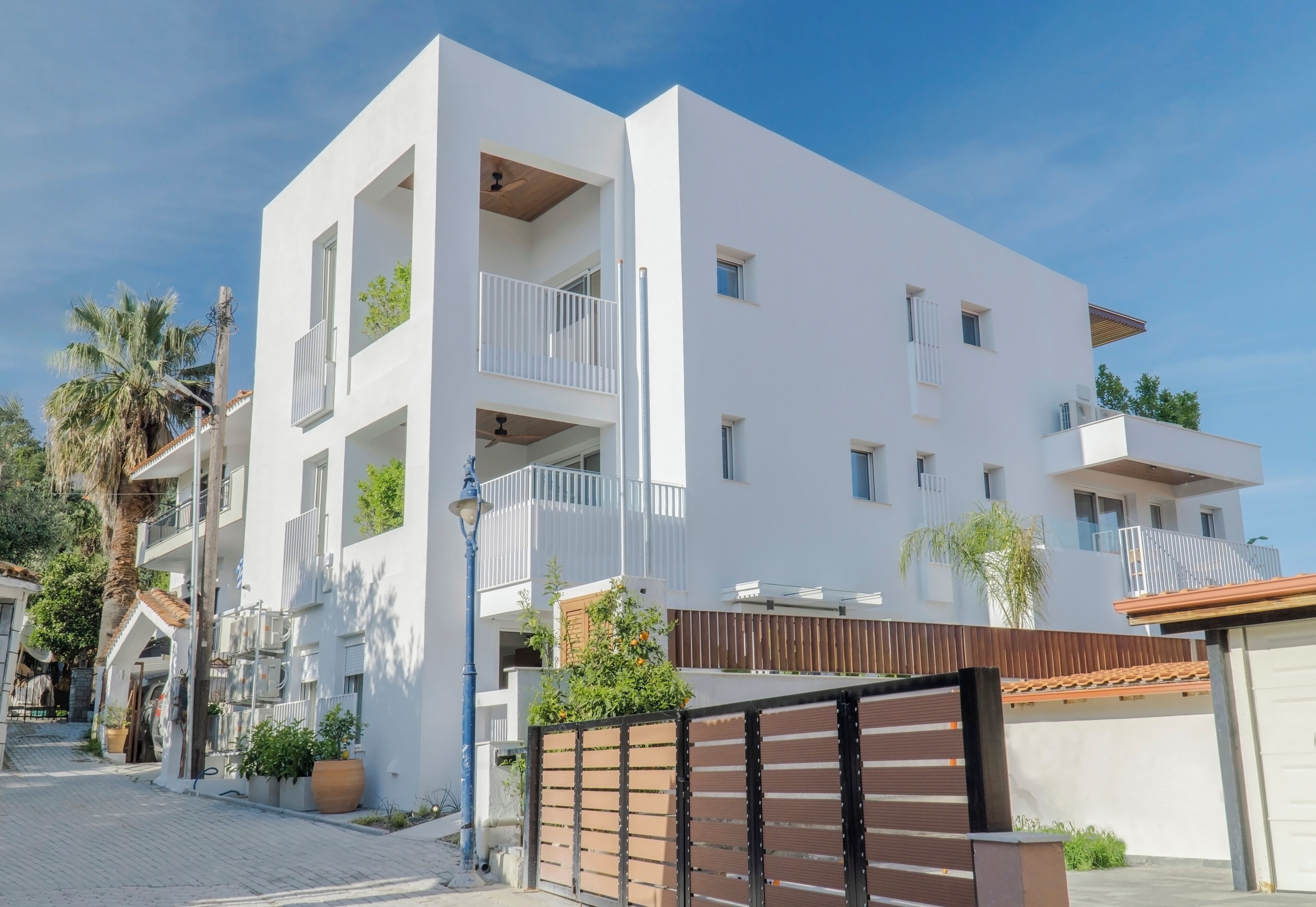 A modern multi-story building with balconies, a gated entrance, and potted plants.