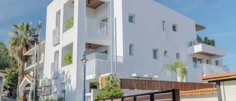 A modern multi-story building with balconies, a gated entrance, and potted plants.