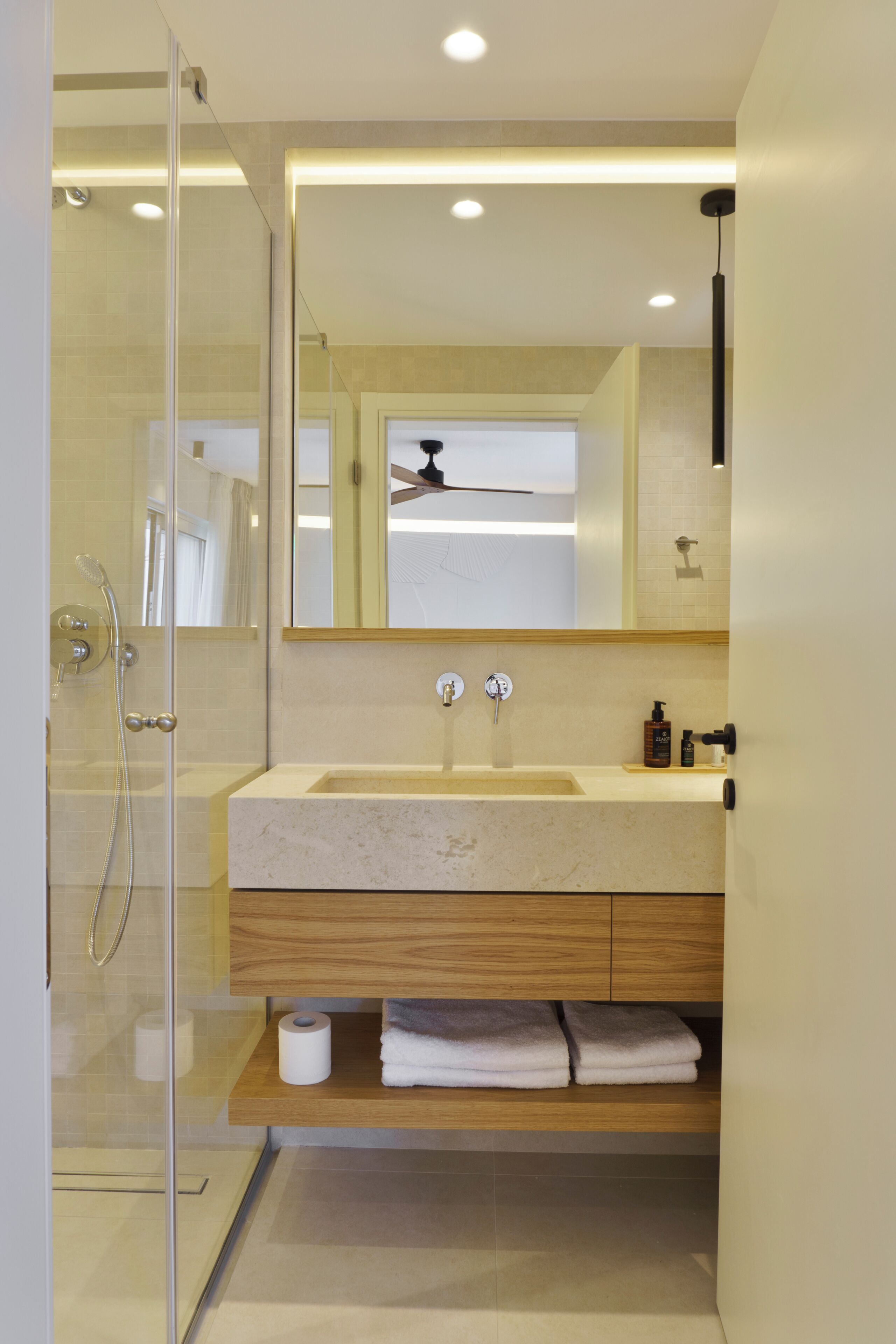 Een moderne badkamer met een glazen douchecabine, een houten wastafelmeubel met een wastafel en een spiegel erboven.