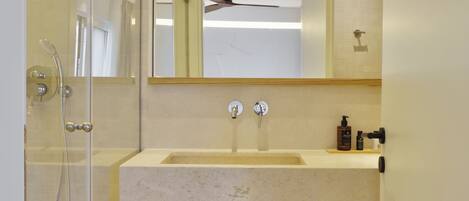 Een moderne badkamer met een glazen douchecabine, een houten wastafelmeubel met een wastafel en een spiegel erboven.