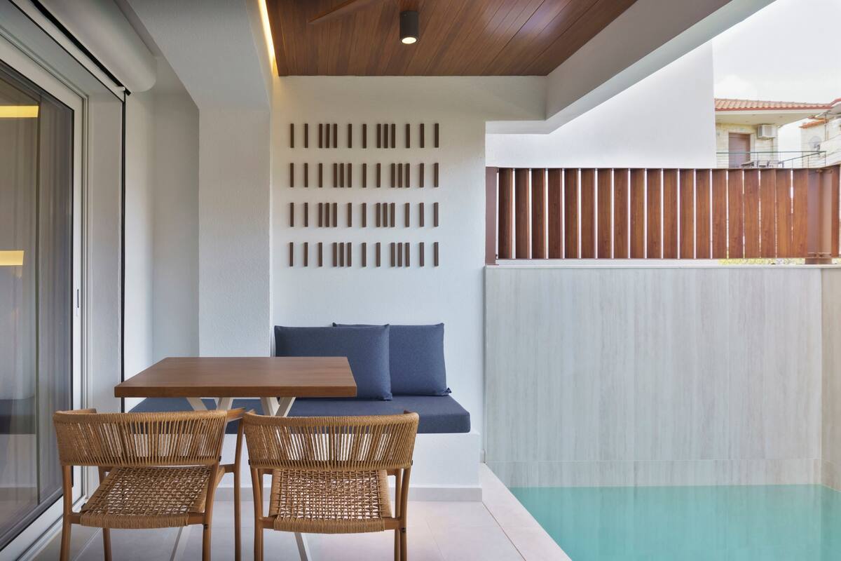 Un interior moderno con techo de madera, puerta de vidrio, sofá con cojines azules, mesa de madera y dos sillas de mimbre.