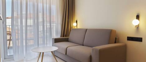 A modern living room with a sofa, a small round table, and a sliding glass door with sheer curtains.