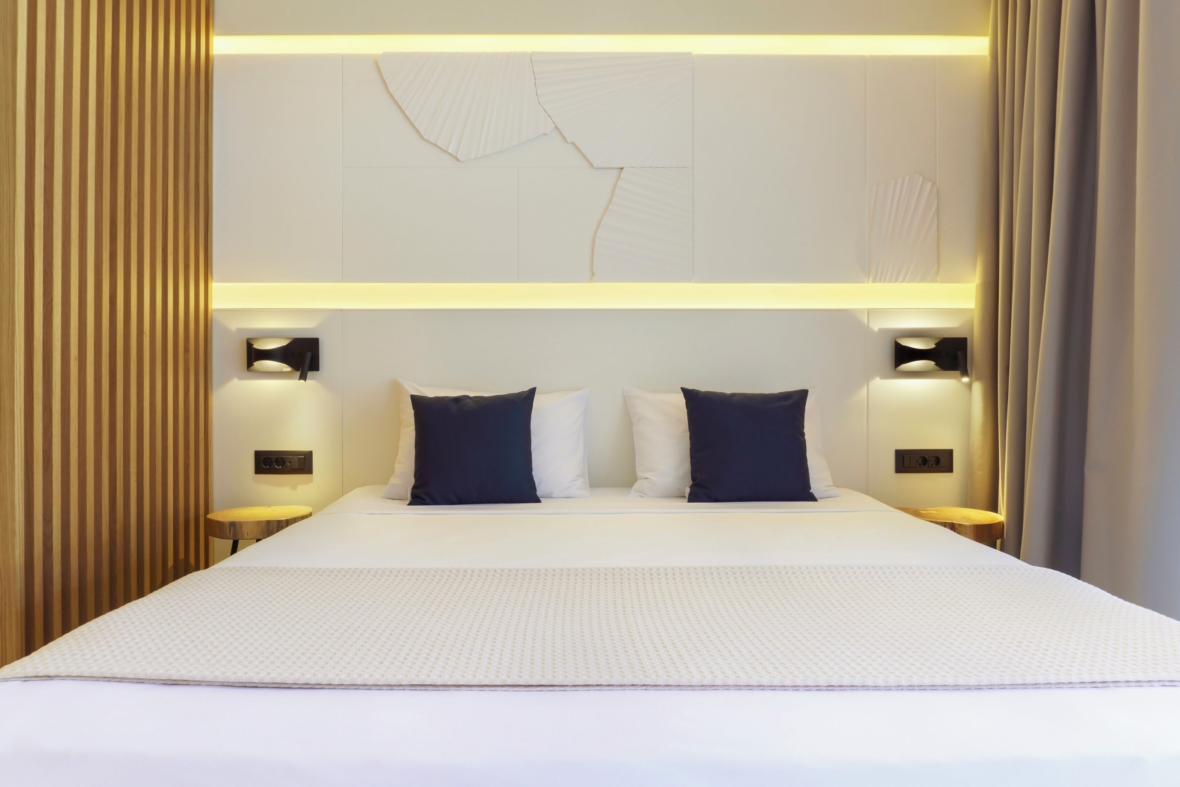 A modern hotel room with a large bed, two bedside tables, and a wall-mounted light fixture.