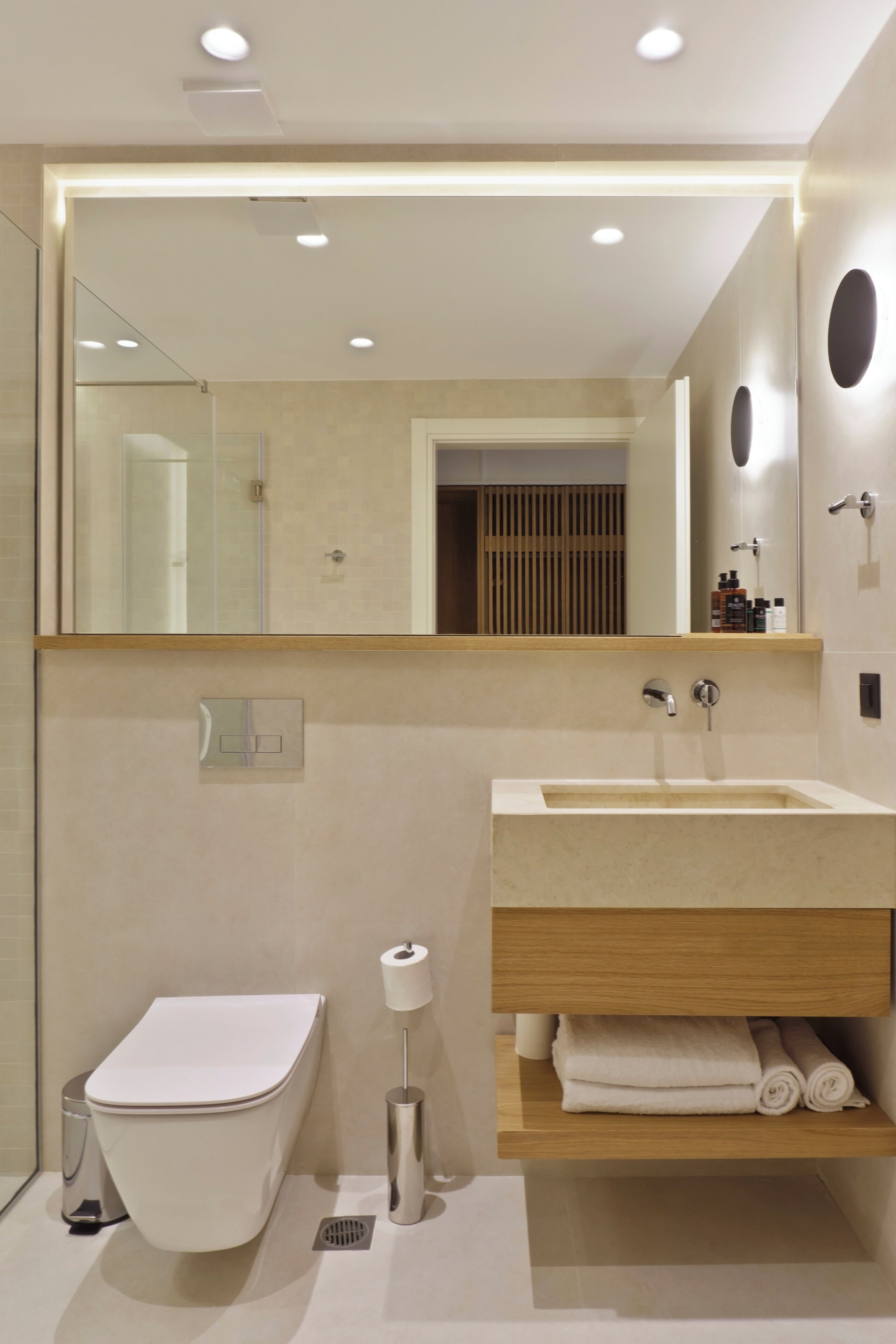 Un baño moderno con inodoro, lavamanos, espejo y espacio para toallas.