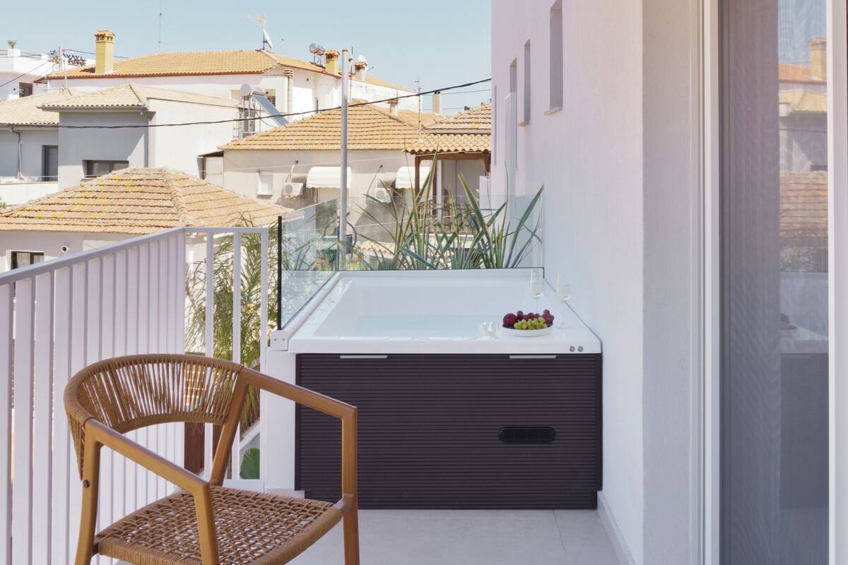 Un balcón con techo de madera, una silla de mimbre, una mesa redonda y vistas a edificios.