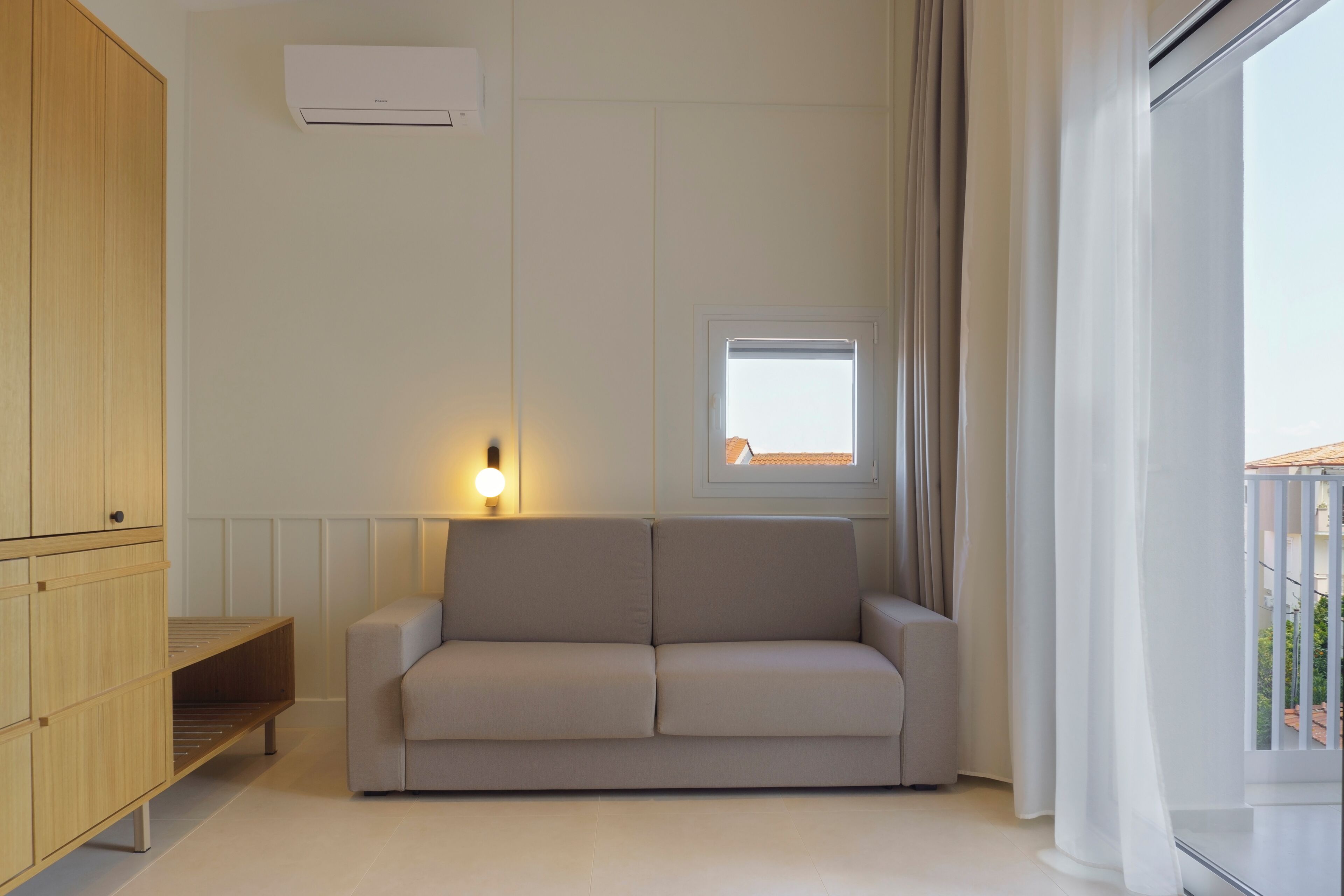 Una sala moderna con un sofá, un aparador de madera, un ventanal pequeño y un balcón con barandilla.
