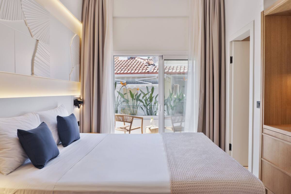 Habitación de hotel con una cama grande, un balcón con plantas y vistas al exterior.