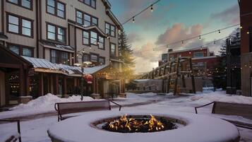 A snow-covered outdoor area with a fire pit, benches, and string lights.