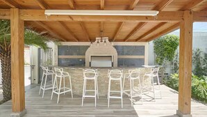 Eine Terrasse im Freien mit einem Steinkamin, einer Holzbalkendecke und weißen Metallbarhocker.