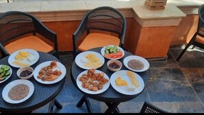 Deux tables rondes, recouvertes d’assiettes remplies de nourriture, et des chaises dotées de coussins orange.