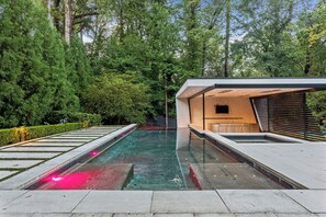 A modern outdoor pool with a glass enclosure, surrounded by lush greenery and a contemporary building structure. - Contemporary Modern estate in delightful Atlanta with an infinity swimming pool (Atlanta)